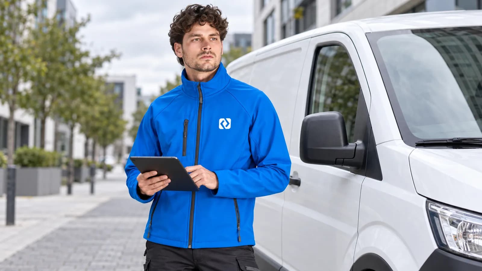 Servisní technik v modré softshellové bundě s logem na hrudi u dodávky